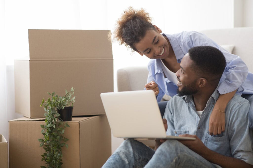 spouses using laptop computer sitting on sofa in new house